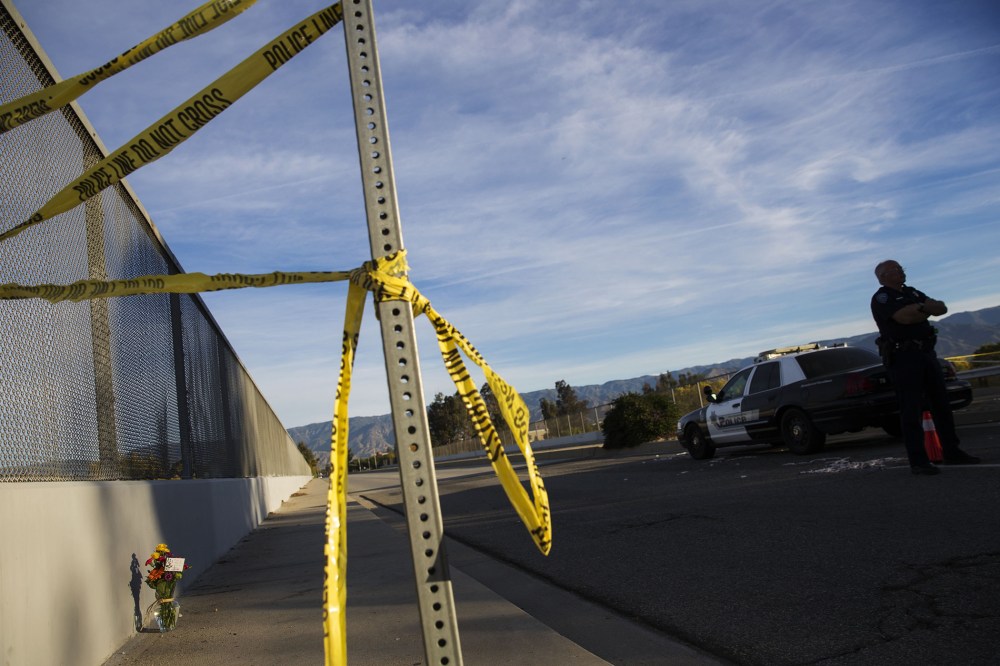A San Bernardino police officer stands on the perimeter as crime scene tape and flowers rest near the Inland Regional Center on Dec. 3, 2015 in San Bernardino, Calif. (Photo by Patrick T. Fallon/AFP/Getty)