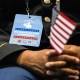 A person seated, focus is on a badge they're wearing that reads "naturalization candidate" as they hold an American flag