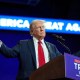 Donald Trump stands at a podium and extends his arms