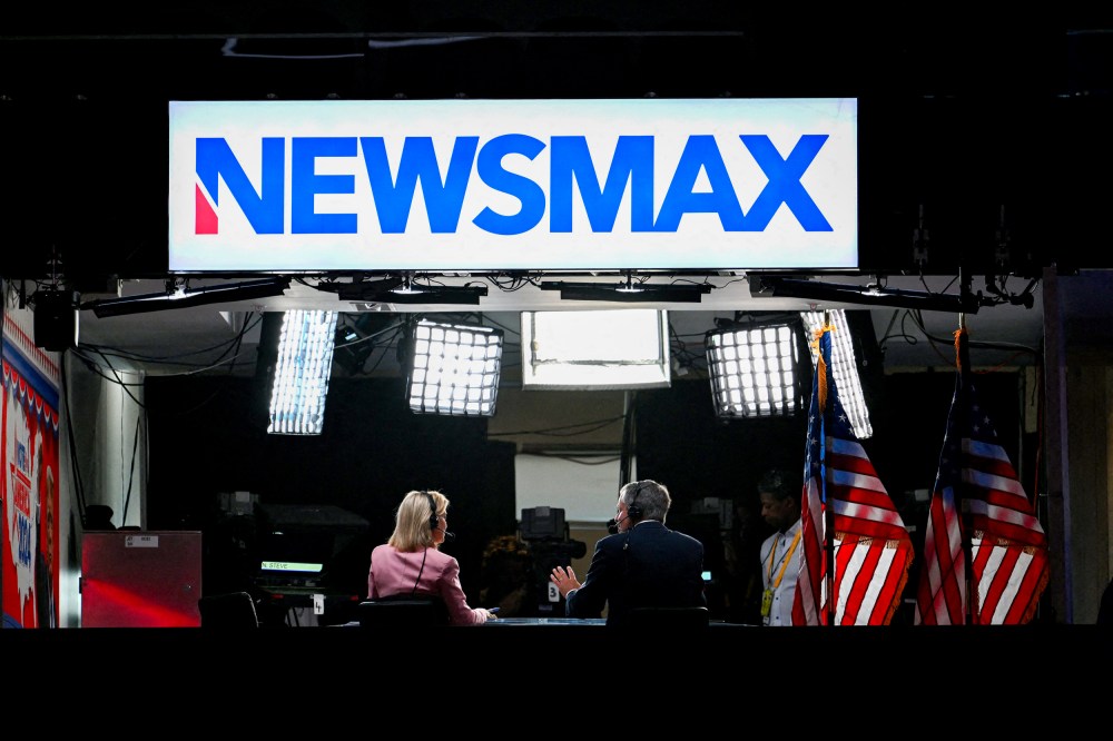 News anchors work at Newsmax's booth.