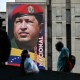 People walk past a mural of Hugo Chavez on the side of a building outside