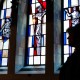 Pastor stands silhouetted by stained glass windows.