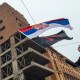 A demonstrator waves the Serbian flag in in Belgrade, Serbia, in front of a run-down building.