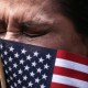 A woman tears up with a small American flag obscuring part of her face.
