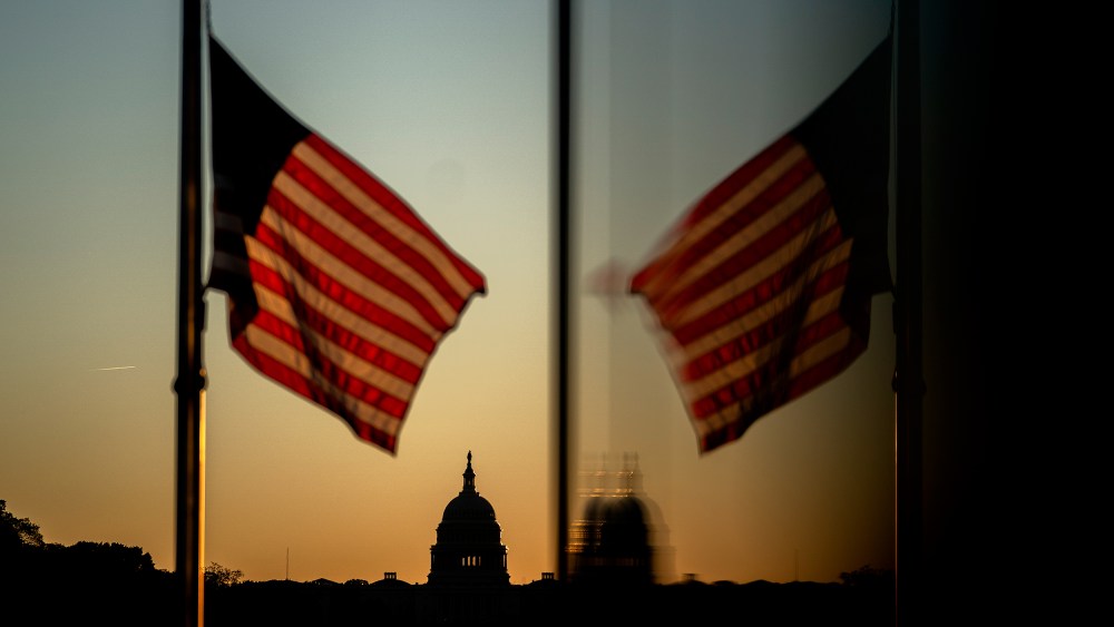 At sunset, an American flag flies in the foreground with the Capitol in focus in the background.