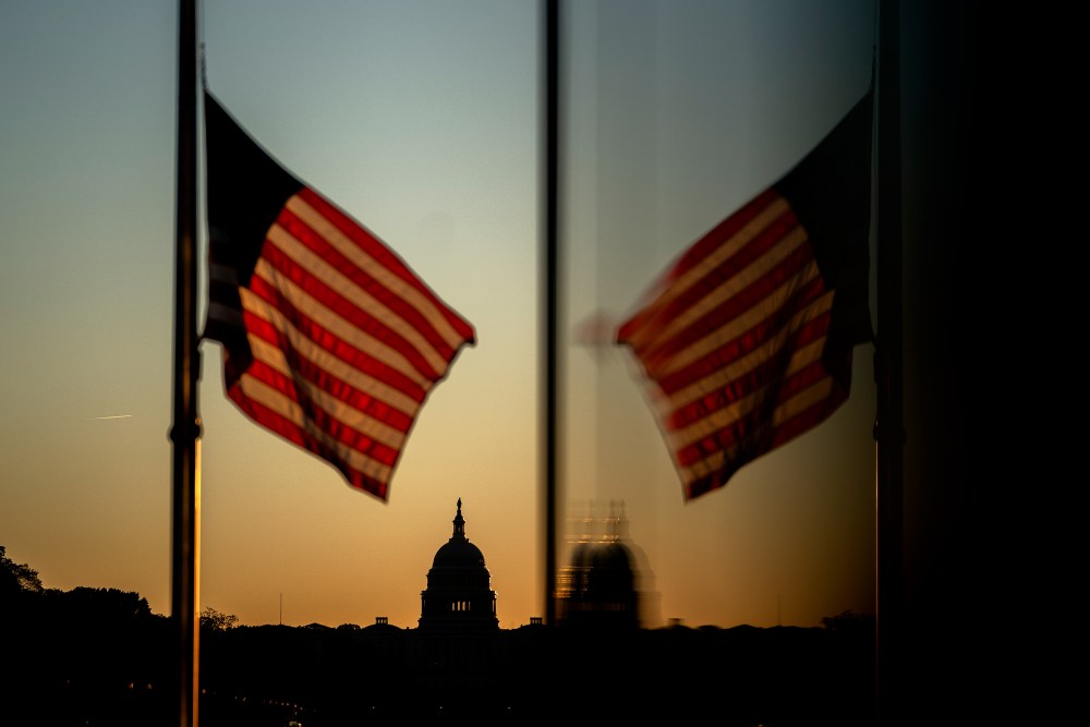 At sunset, an American flag flies in the foreground with the Capitol in focus in the background.