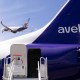 Part of an Avelo airplane is seen in the foreground; an Avelo airplane takes off in the background.