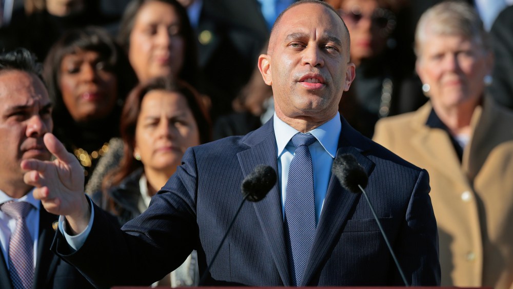 Hakeem Jeffries stands at a podium in front of a crowd of other Democratic leaders.