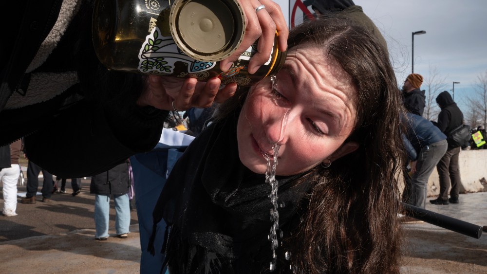 An unseen person pours water from a reusable water bottle into another person's eyes.