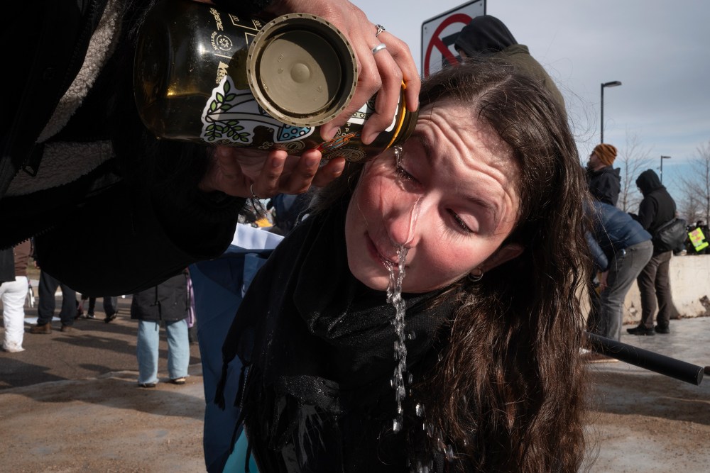 An unseen person pours water from a reusable water bottle into another person's eyes.