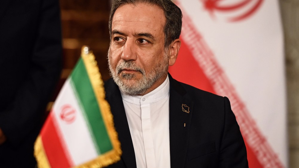 Iranian Foreign Minister Abbas Araghchi with an Iranian flag in front of him and behind him.