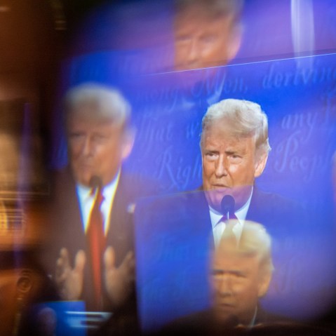 A window, acting as a prism, multiplies an image of Donald Trump on a TV.