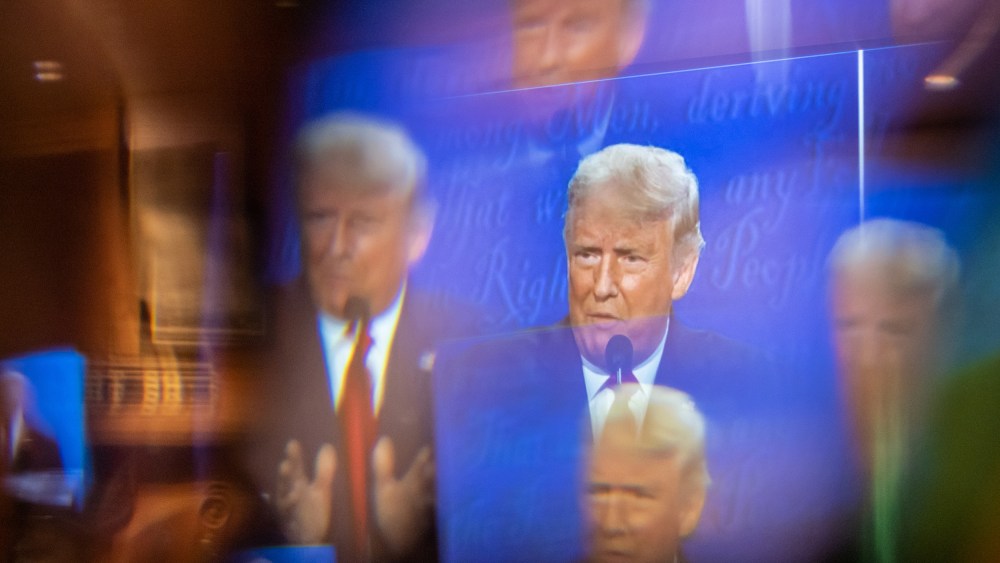 A window, acting as a prism, multiplies an image of Donald Trump on a TV.