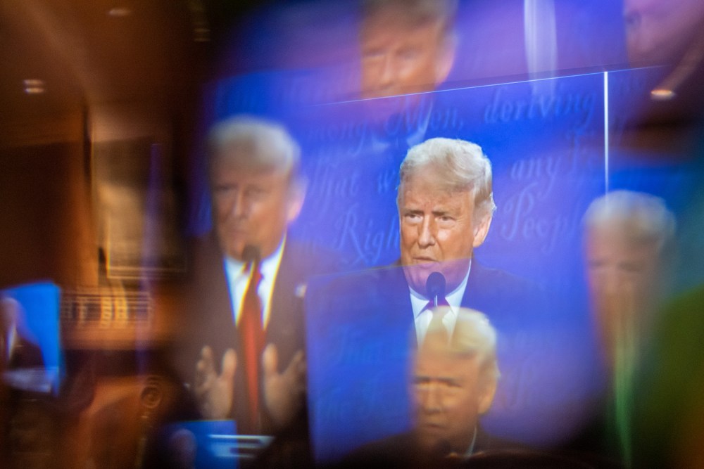 A window, acting as a prism, multiplies an image of Donald Trump on a TV.