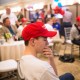 A young man wearing a "Make America Great Again" hat puts his hand to his face.