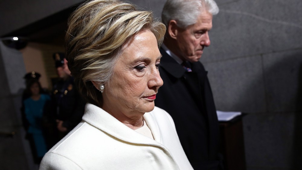 Profiles of Hillary Clinton (foreground) and Bill Clinton (background), both looking down.