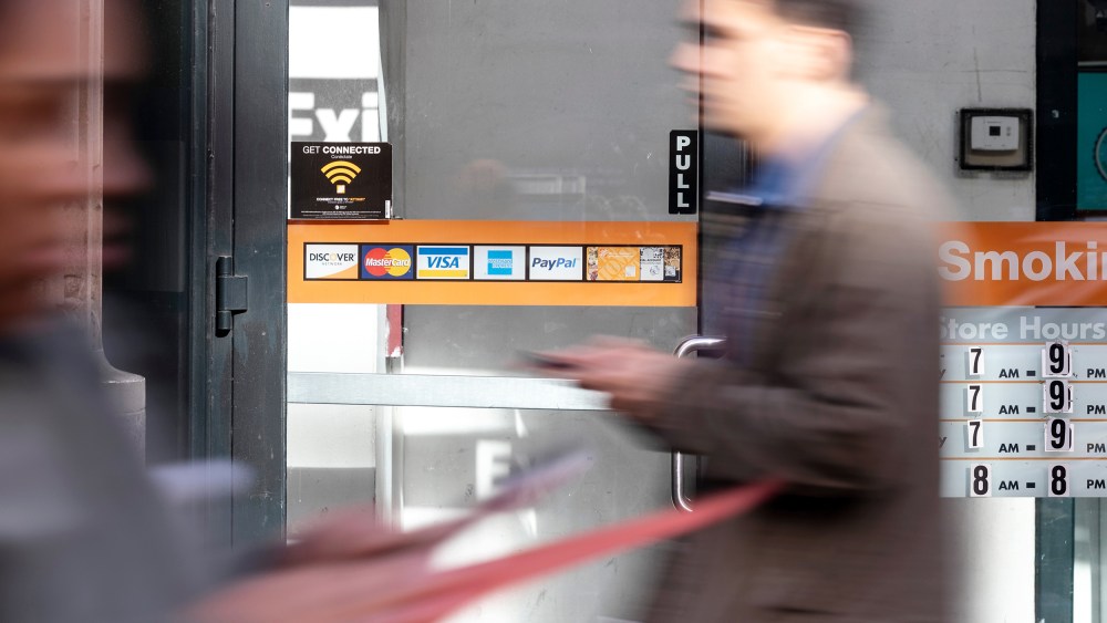 Credit card stickers are seen on a store window while two people pass by.