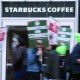 People blurred in motion hold signs in front of a Starbucks Coffee location.