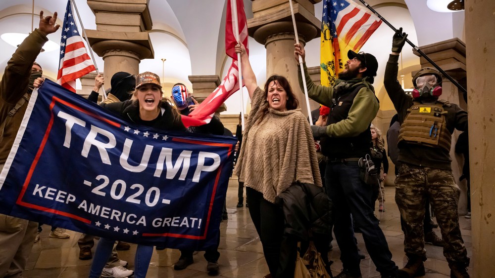 People within the Capitol hold flags supporting Donald Trump.
