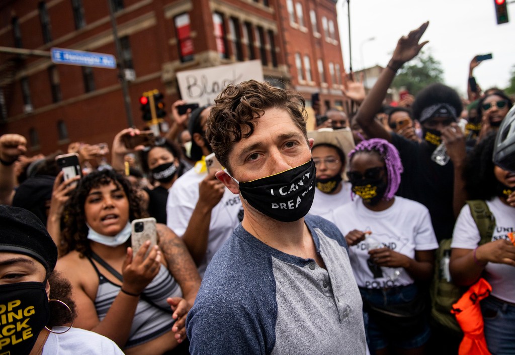 Minneapolis mayor Jacob Frey stands in front of demonstrators, wearing a mask that reads 