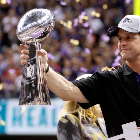 John Harbaugh holds the Vince Lombardi Championship trophy as purple and gold confetti falls in the background.