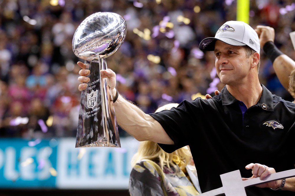 John Harbaugh holds the Vince Lombardi Championship trophy as purple and gold confetti falls in the background.