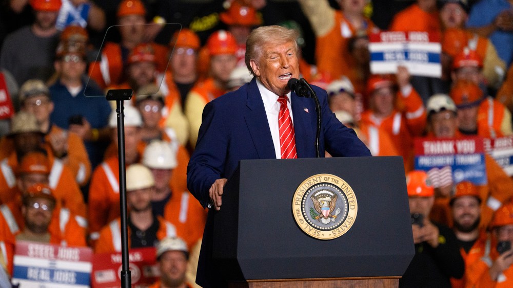 President Donald Trump speaks at a podium in front of audience members, many of whom are in orange vests and hard hats.