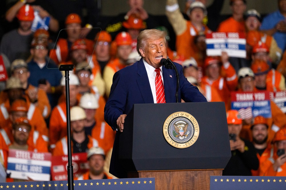 President Donald Trump speaks at a podium in front of audience members, many of whom are in orange vests and hard hats.