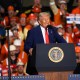President Donald Trump speaks at a podium in front of audience members, many of whom are in orange vests and hard hats.