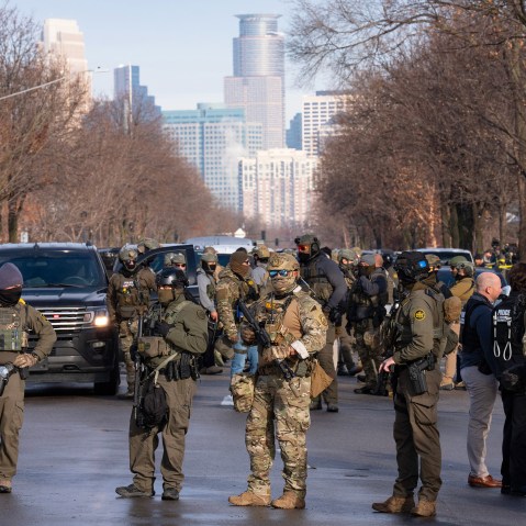 Federal agents stand in the street with the a partial view of the Minneapolis skyline in the background.