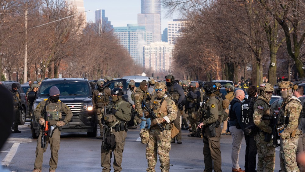 Federal agents stand in the street with the a partial view of the Minneapolis skyline in the background.