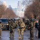 Federal agents stand in the street with the a partial view of the Minneapolis skyline in the background.