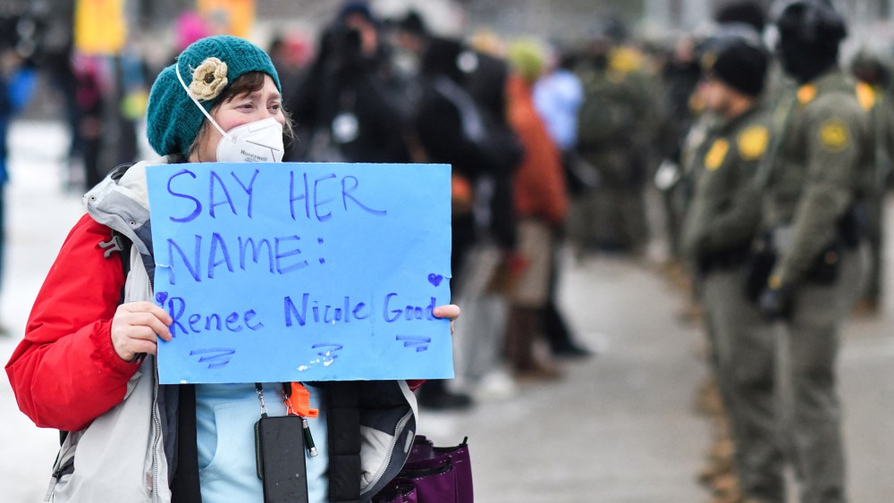 A protestor holds a sign as federal agents stand guard as protestors gather outside the Bishop Henry Whipple Federal Building in Saint Paul, MN.