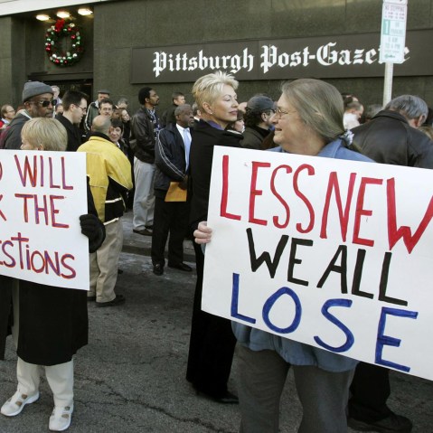 People hold signs reading "Who will ask the questions" and "Less news we all lose" outside the Pittsburgh Post-Gazette building.