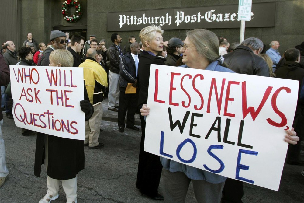 People hold signs reading "Who will ask the questions" and "Less news we all lose" outside the Pittsburgh Post-Gazette building.