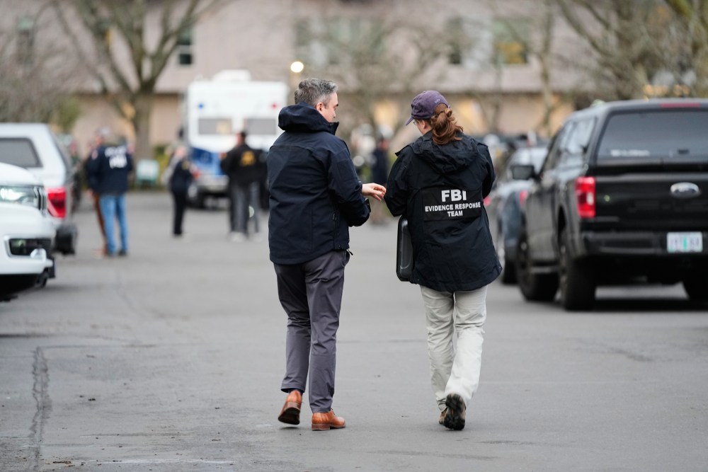 Two people, one in an FBI jacket, walk away from the camera in the street.