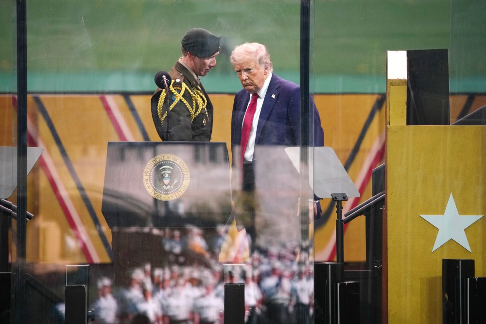 President Trump talks to a member of the U.S. military on the podium as a parade goes on.