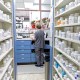 A pharmacy employee faces away from the camera by shelves with prescription drugs.