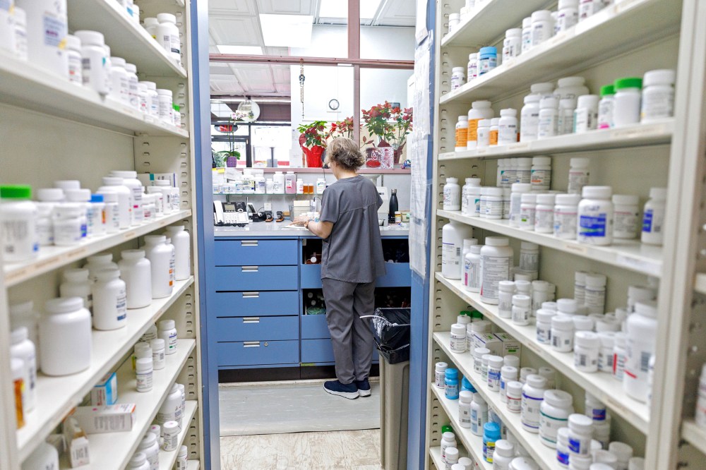A pharmacy employee faces away from the camera by shelves with prescription drugs.