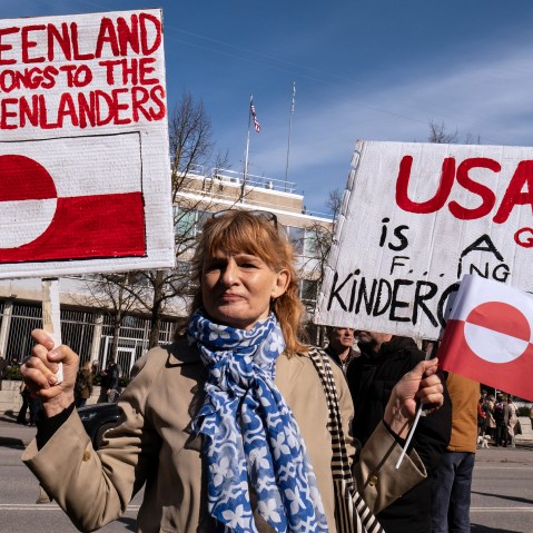 A person holds signs condemning U.S. pressure on Greenland and Denmark.
