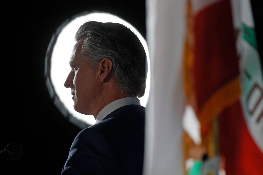 Gavin Newsom backlit, next to a California state flag.