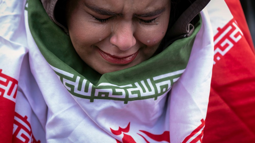 A young woman, wrapped in an Iranian flag, cries.