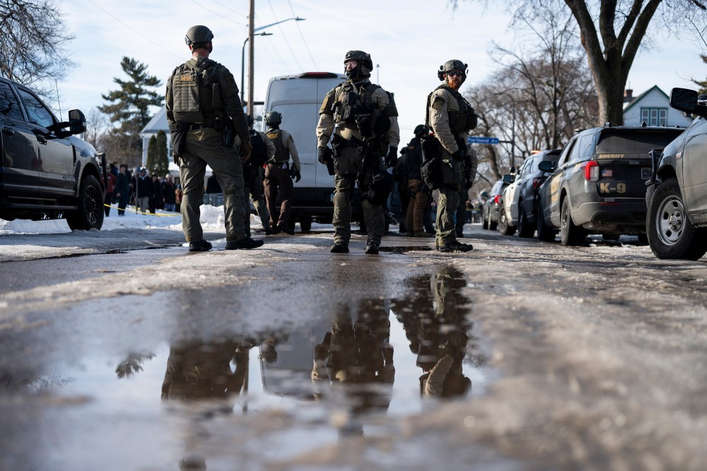 Law enforcement and officers stand in the street.