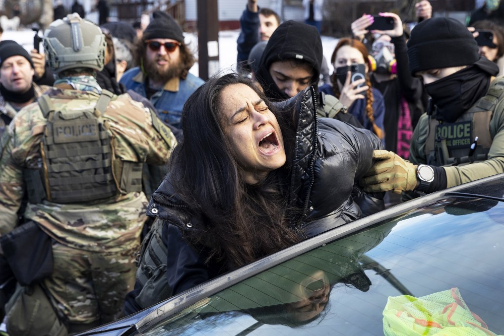 Federal Agents arrest a woman after smashing her car windows for allegedly blocking the street during an immigration enforcement operation on Jan. 13, 2026, in Minneapolis.