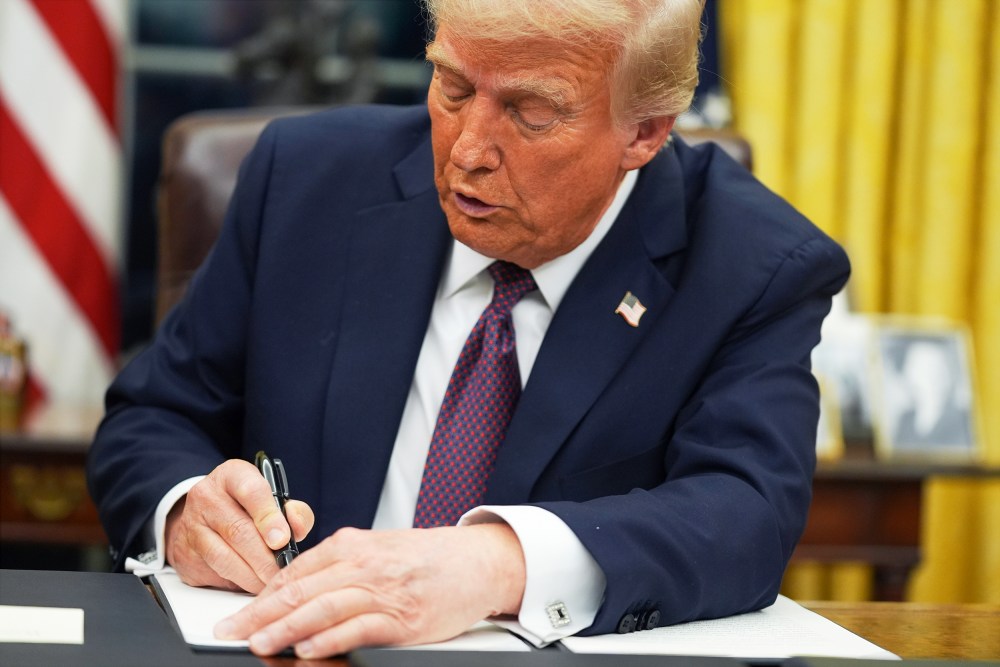 President Donald Trump signs a document at his desk.