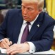 President Donald Trump signs a document at his desk.