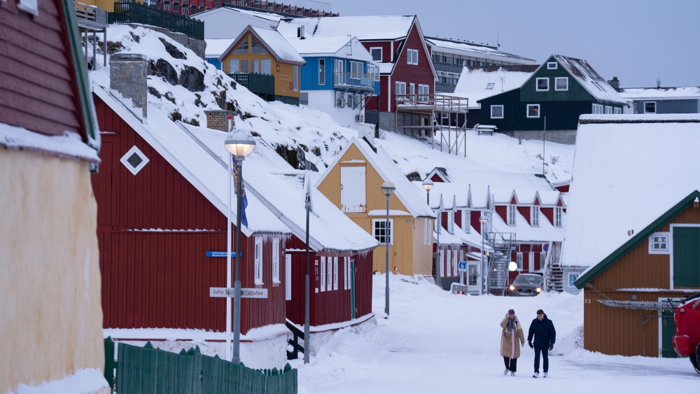 Two people walk among brightly painted houses in the snow.