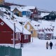 Two people walk among brightly painted houses in the snow.