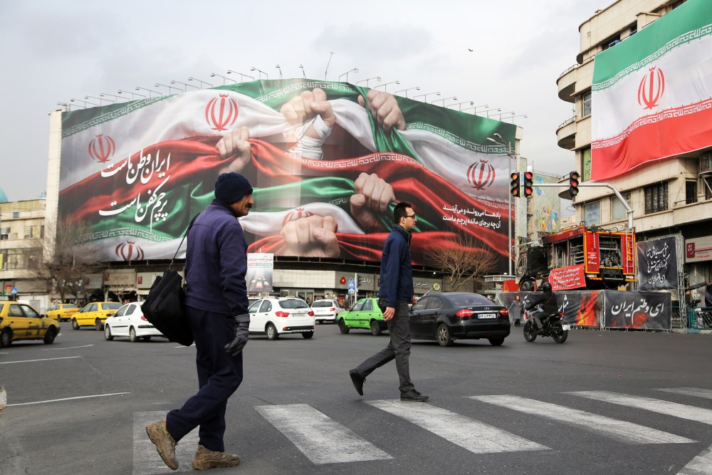 A photo showing daily life in Tehran where two men crossing the street with a big iranian flag seen on a billboard in the background.