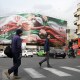 A photo showing daily life in Tehran where two men crossing the street with a big iranian flag seen on a billboard in the background.
